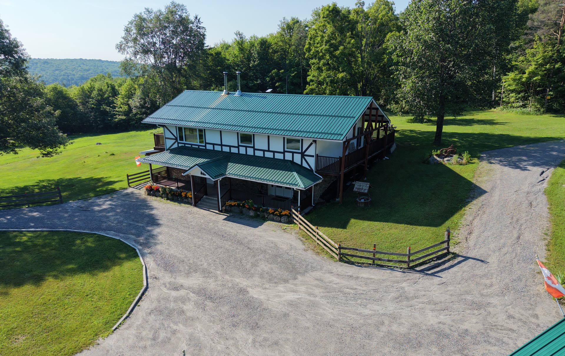 Sunny aerial view of the 497 Mooney Road homestead, its wraparound decks and circular drive on 141 acres